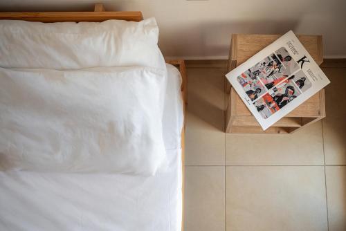 a bed with white sheets and a magazine on a night stand at Light House Chania - 5 Min to Beach and Free Parking in Chania Town