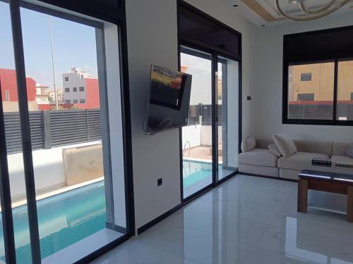 a living room with a couch and a tv and windows at Villa Chez Badre with Pool High Standing in Sidi Rahal