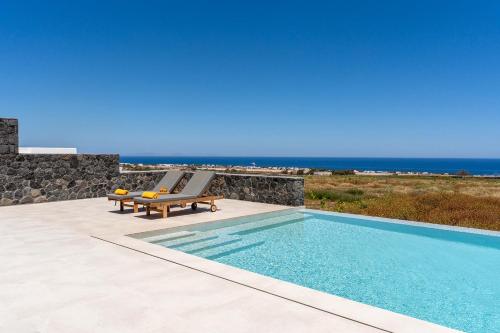 a swimming pool with two lounge chairs and the ocean at Platies Luxury Apartments Santorini in Éxo Goniá