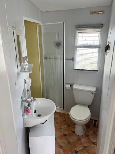 a white bathroom with a toilet and a sink at Kings Caravan Park A-56 in Chapel Saint Leonards