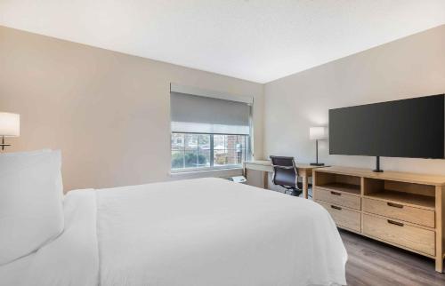 a white bedroom with a bed and a desk with a television at Extended Stay America Suites - Washington, DC - Fairfax - Fair Oaks Mall in Fairfax