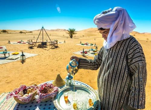 eine Frau in der Wüste mit einem Tablett mit Essen in der Unterkunft Alwan Luxury Camp in Merzouga