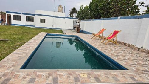 a swimming pool with two chairs and a house at Casa de campo relax y piscina in Cerro Azul