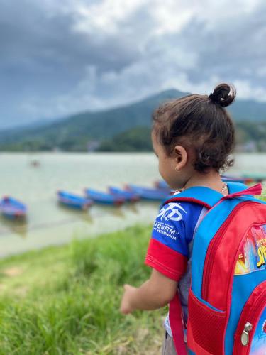 a little girl with a backpack looking at the water at Hotel Royal Orbit Pvt Ltd Pokhara in Pokhara