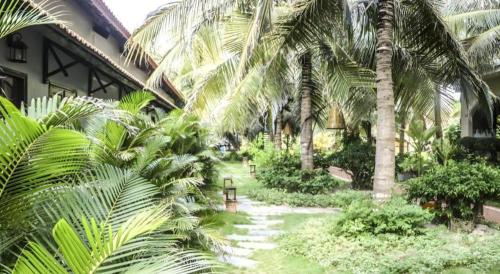 a garden with palm trees in front of a building at HON BA LAGI BEACH RESORT in La Gi