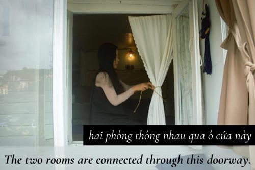 a woman looking out of a window with a curtain at Cú Trên Cây Homestay in Xuan An