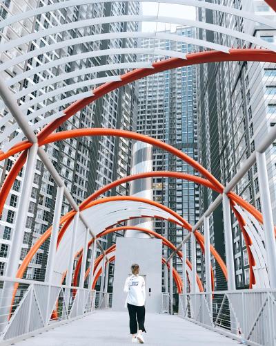 a woman walking across a bridge in front of tall buildings at The Peak Suite at Landmark Plus in Ho Chi Minh City