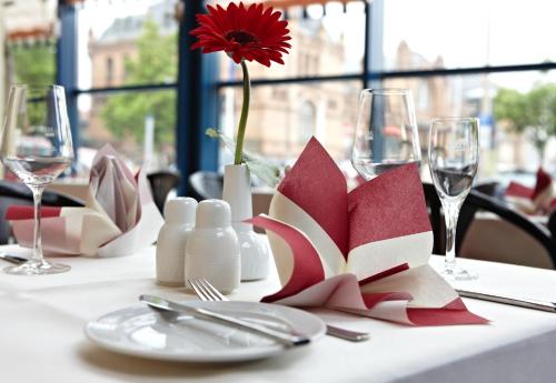 a table with a red flower in a vase on a table with glasses at IntercityHotel Schwerin in Schwerin