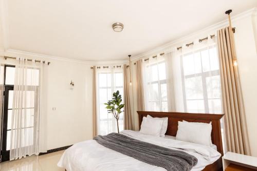 a bedroom with a bed with white sheets and windows at kigali Pillar House inn in Kigali