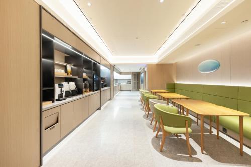 una cafetería con mesas de madera y sillas verdes en JI Hotel Beijing Capital Economic and Trade Jijiamiao Subway Station, en Beijing