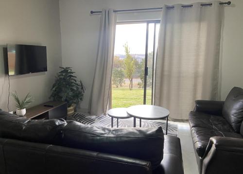 Una sala de estar con un sofá y una mesa y una ventana. en Warm, Homely Apartment - 5min Away Menlyn Main, en Pretoria
