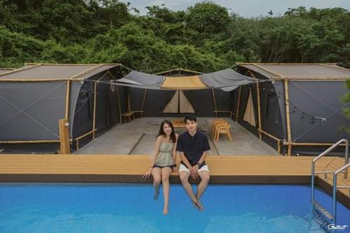 a man and woman sitting on the edge of a pool with tents at The X10 Nordic Tent and Glamping Pool Villa Khaoyai เขาใหญ่ - SHA Certified in Ban Thung Sawang