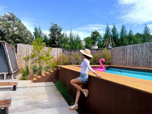 a woman in a hat sitting on a fence next to a swimming pool at The X10 Nordic Tent and Glamping Pool Villa Khaoyai เขาใหญ่ - SHA Certified in Ban Thung Sawang