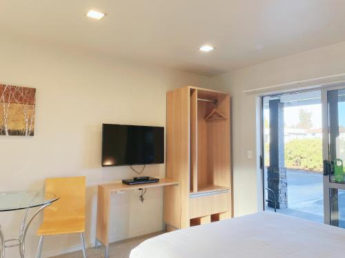 a bedroom with a bed and a tv and a table at Anchorage Motel Apartments in Te Anau