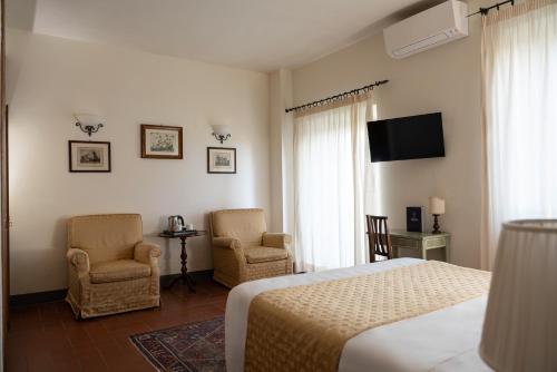 a bedroom with a bed and two chairs and a television at Relais Vignale & Spa in Radda in Chianti