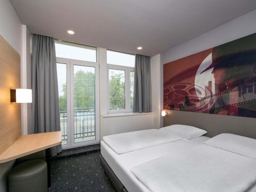 a hotel room with a bed and a desk and window at B&B HOTEL Berlin-Adlershof in Berlin