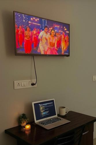 a laptop on a desk with a tv on the wall at The First Floor I Top Rated Boutique Homestay I Near Lekhraj Metro Lucknow in Lucknow