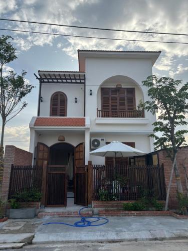 a white house with a fence and an umbrella at à Bleu Hoian in Tân Thành (1)