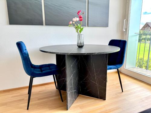 a black table with blue chairs and a vase with flowers at FLAIR Apartments Vorarlberg - Stilvolles Wohnen nahe Bodensee & Alpen - Küche, Balkon & Gratis Parkplatz in Bregenz