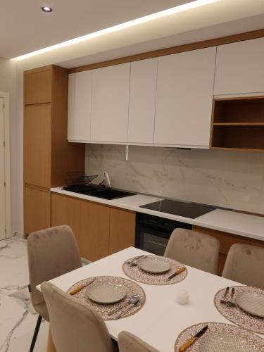 a kitchen with a table with chairs and white cabinets at Marbel Apartments 1 in Shëngjin