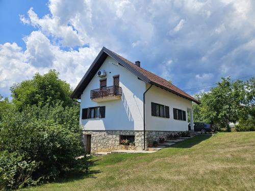 a white house with a balcony on a field at Cherry Hill Loft in Plitvička Jezera