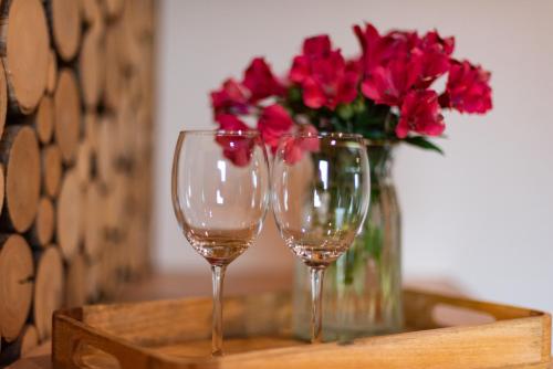 two wine glasses on a wooden tray with a vase of red flowers at Ośrodek Wypoczynkowy Bernadetta in Murzasichle