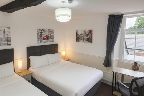 a bedroom with two beds and a desk and a window at The Swan Hotel Oxford in Eynsham