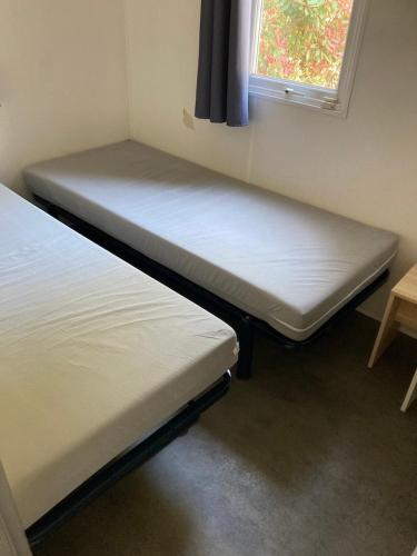 two beds in a small room with a window at Bonne Anse plage 411 mobile home 3 chambres in Les Mathes