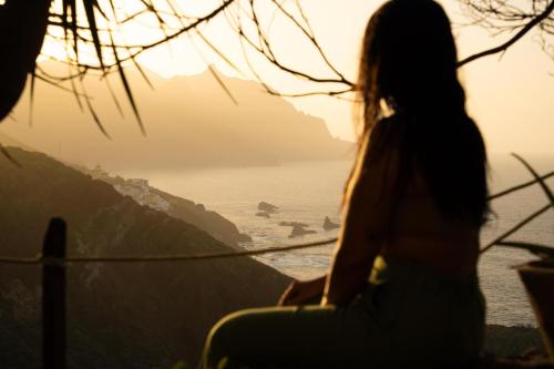 a woman sitting on a ledge looking out at the ocean at Casa Amarilla de Playa Benijo in Almáciga