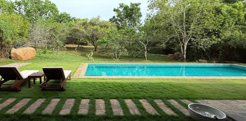 a swimming pool with two chairs and a table in the grass at Nyne Hotels Mayur Lodge - Yala - All Inclusive in Yala