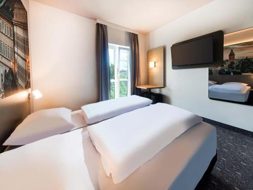 a hotel room with two beds and a flat screen tv at B&B HOTEL Gotha-Hbf in Gotha