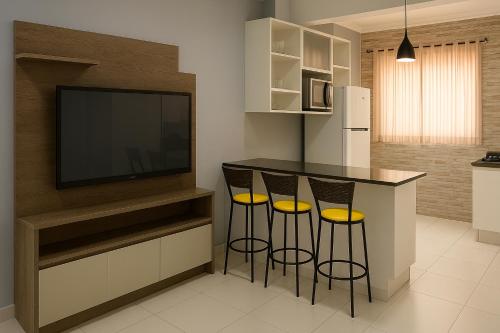 a kitchen with a bar with three stools and a television at Apartamento Cantinho da Cop 30 in Ananindeua