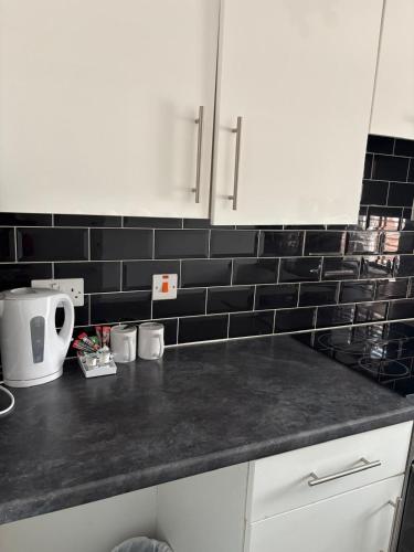 a kitchen with white cabinets and black tiles on the wall at The Tudor House Hotel in Nottingham
