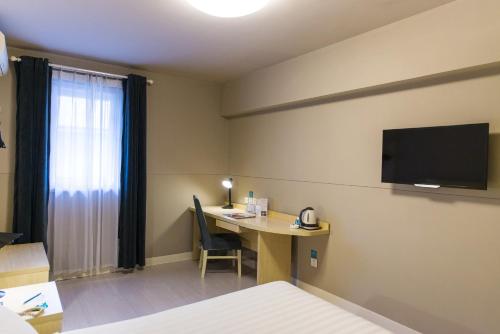 a hotel room with a desk and a tv on the wall at Jinjiang Inn Weihai Shichang Avenue High-speed Train North Station in Weihai