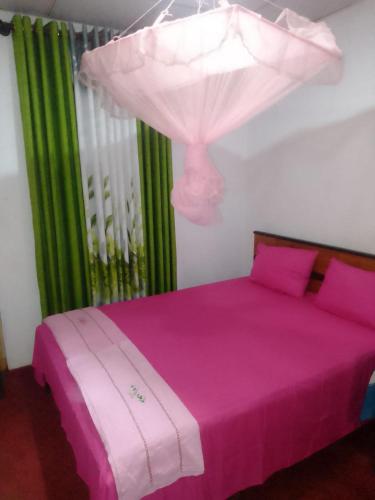 a bedroom with a pink bed with pink sheets and green curtains at Peacock Residence & Cabana's in Tangalle