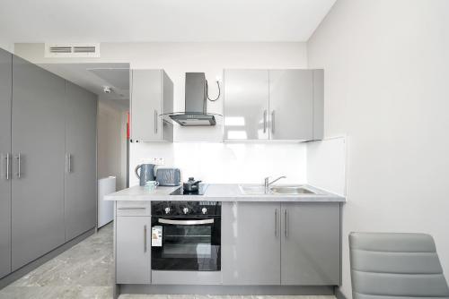 a white kitchen with a sink and a stove at Studio with Balcony Godino Hotel Ilford in Ilford
