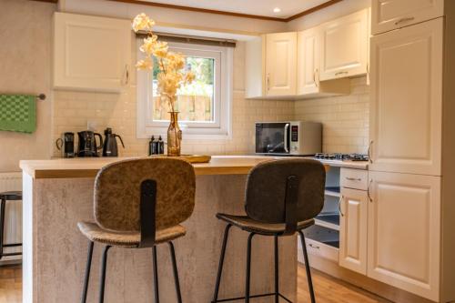 a kitchen with white cabinets and two bar stools at Home 6P Bath-Garden house-4G Pool-Kids-Dog in Hoenderloo
