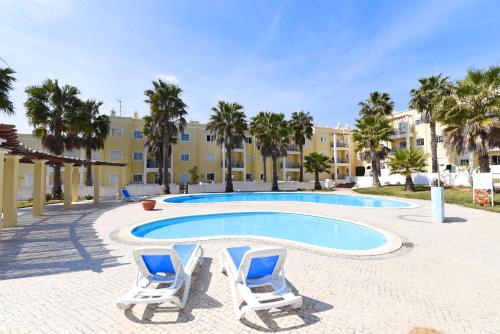 a swimming pool with two lounge chairs and a building at Praia da Lota Resort – Beachfront Apartments in Manta Rota