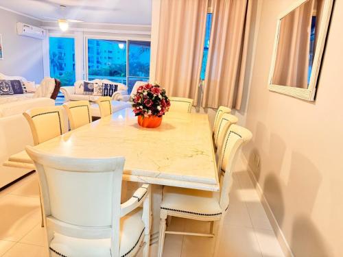 a dining room table with white chairs and a vase of flowers at Riviera de São Lourenço, pé na grama in Bertioga