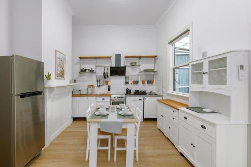 a kitchen with white cabinets and a table with chairs at Cremorne Cottage - MCG, Bars, cafes & Richmond Hub in Melbourne