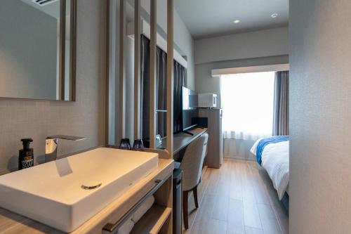 a bathroom with a sink and a bed in a room at HOTEL R9 Premium Kawamataekimae in Ōra