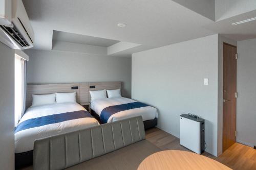 a bedroom with two beds and a couch at HOTEL R9 Premium Kawamataekimae in Ōra