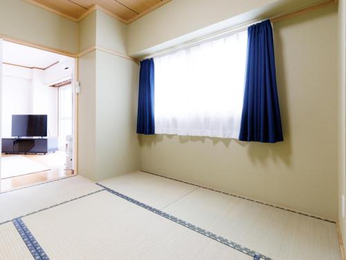 a room with a large window with blue curtains at Tabist JKNツインホテル in Asahikawa