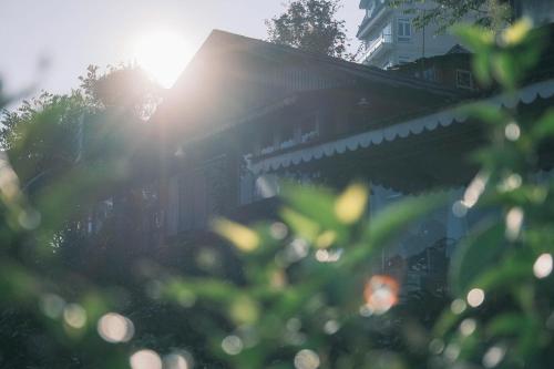 a house with the sun shining through the trees at Cú Trên Cây Homestay in Xuan An
