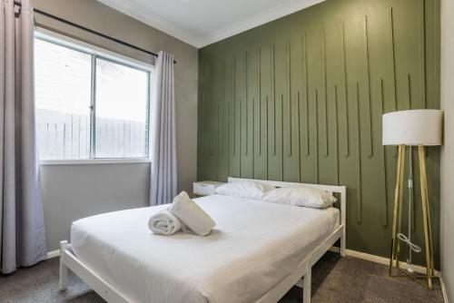 a bedroom with a white bed with a green wall at The Airport Stop Modern, 15min to Brisbane City in Brisbane