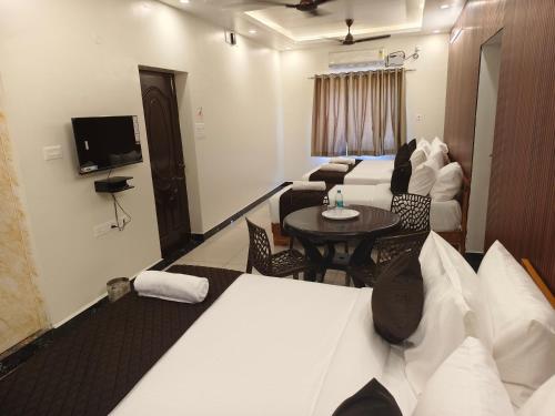 a hotel room with beds and a table and a tv at Sai RBM Grand Inn in Kuilapayam