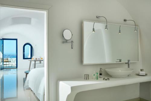 La salle de bains blanche est pourvue d'un lavabo et d'un miroir. dans l'établissement Katikies Chromata Santorini - The Leading Hotels of the World, à Imerovigli