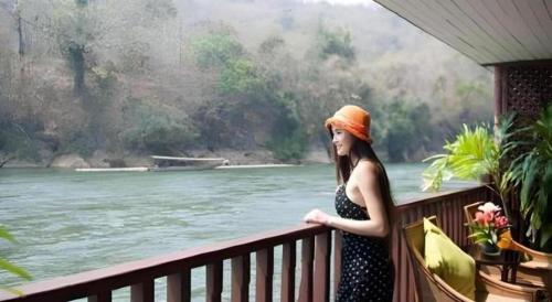 a woman standing on a balcony overlooking a river at River Kwai Village Hotel in Ban Kaeng Raboet