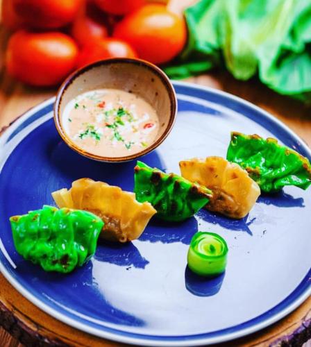 a blue plate with a bowl of dip and green food at Nunia Tamansari Hotel in Kumprung