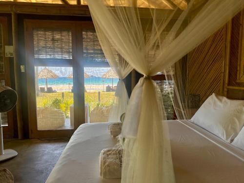a bedroom with a canopy bed with a large window at Eco Sanctuaries Nature Lodge Nacpan Beach, El Nido in El Nido